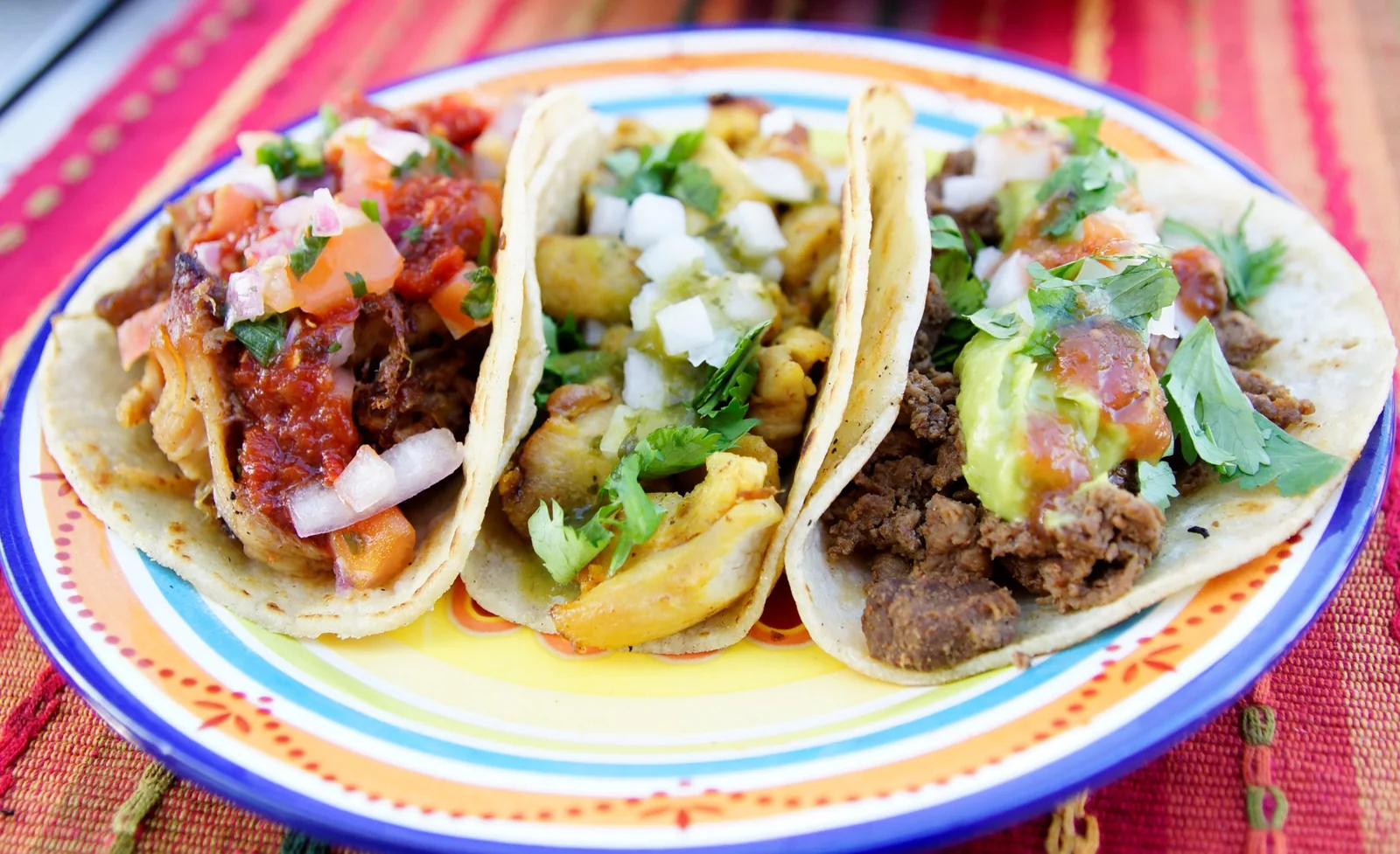 Three tacos on a colorful plate with salsa, cilantro and guacamole